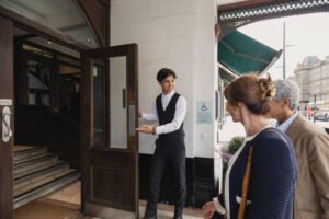 Mature couple are arriving at a hotel and a doorman is welcoming them in.
